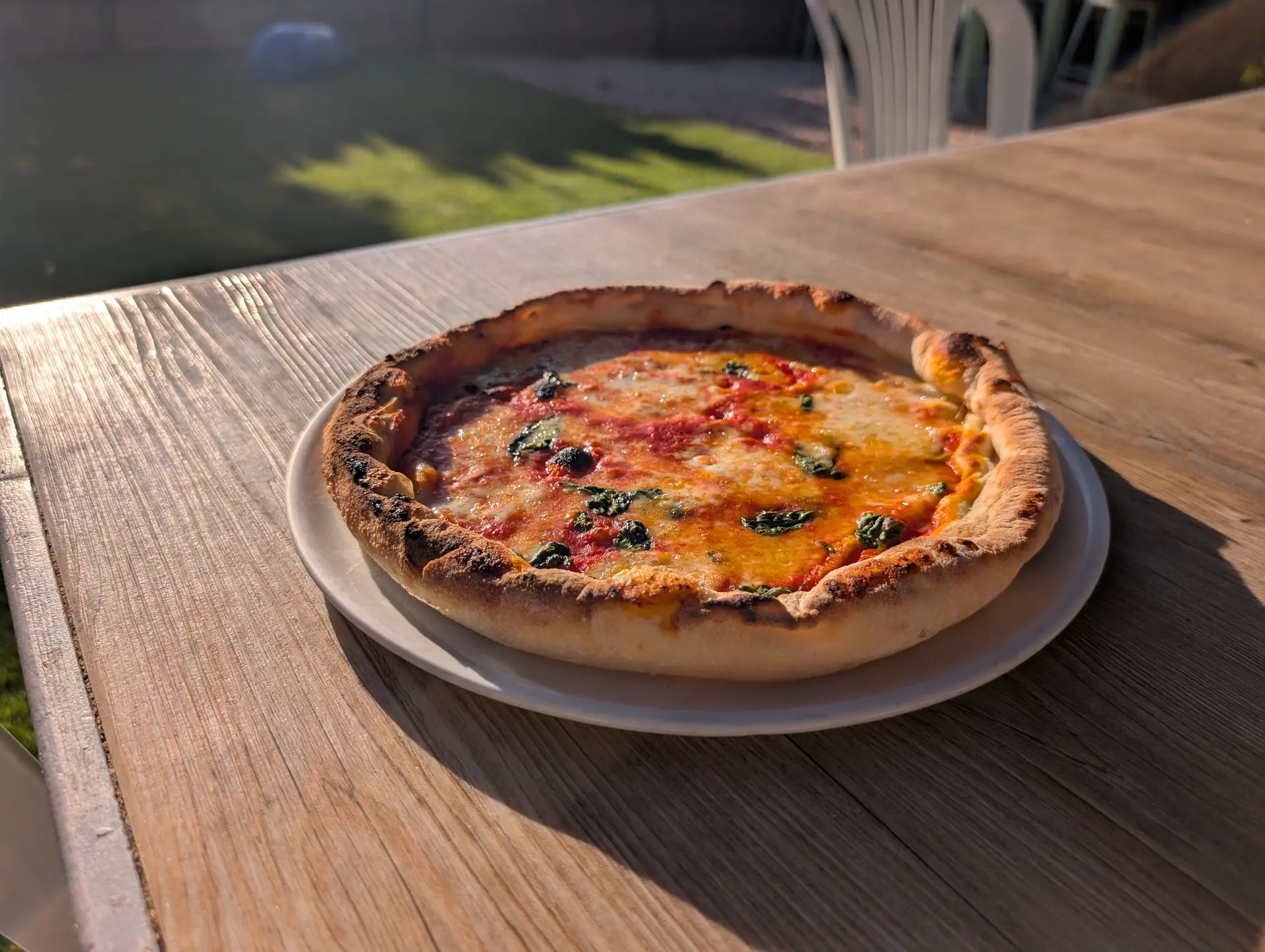 A fresh stone-baked margherita pizza on a wooden outdoor table at Zazoo