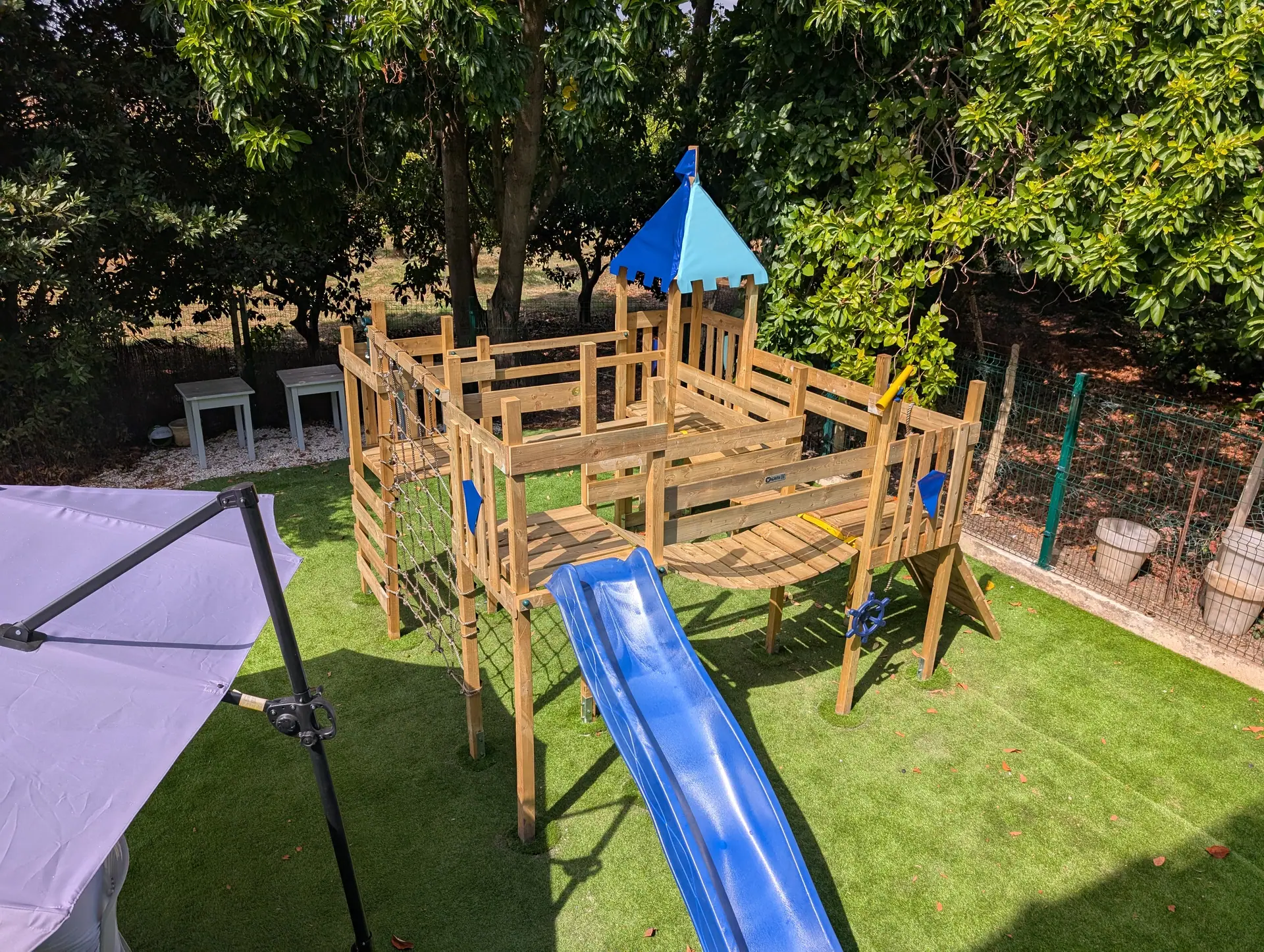 Zazoo's wooden play castle with a blue slide on bright astro turf