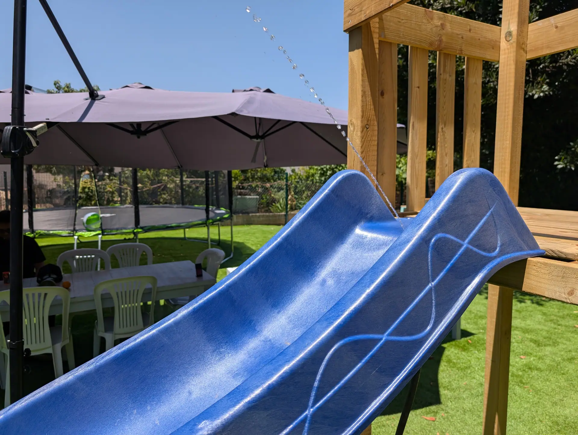 The blue outdoor slide, trampoline and shaded tables in Zazoo's garden