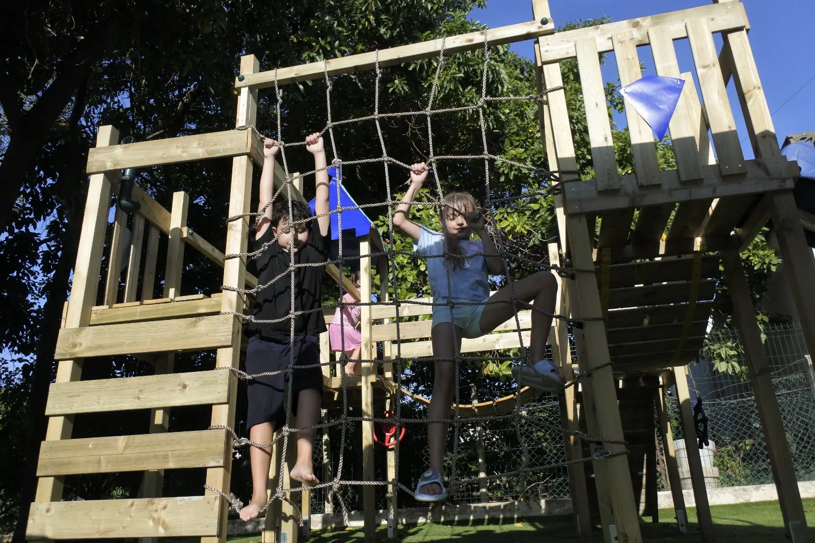 Two children clambering up the cargo net on Zazoo's wooden climbing frame