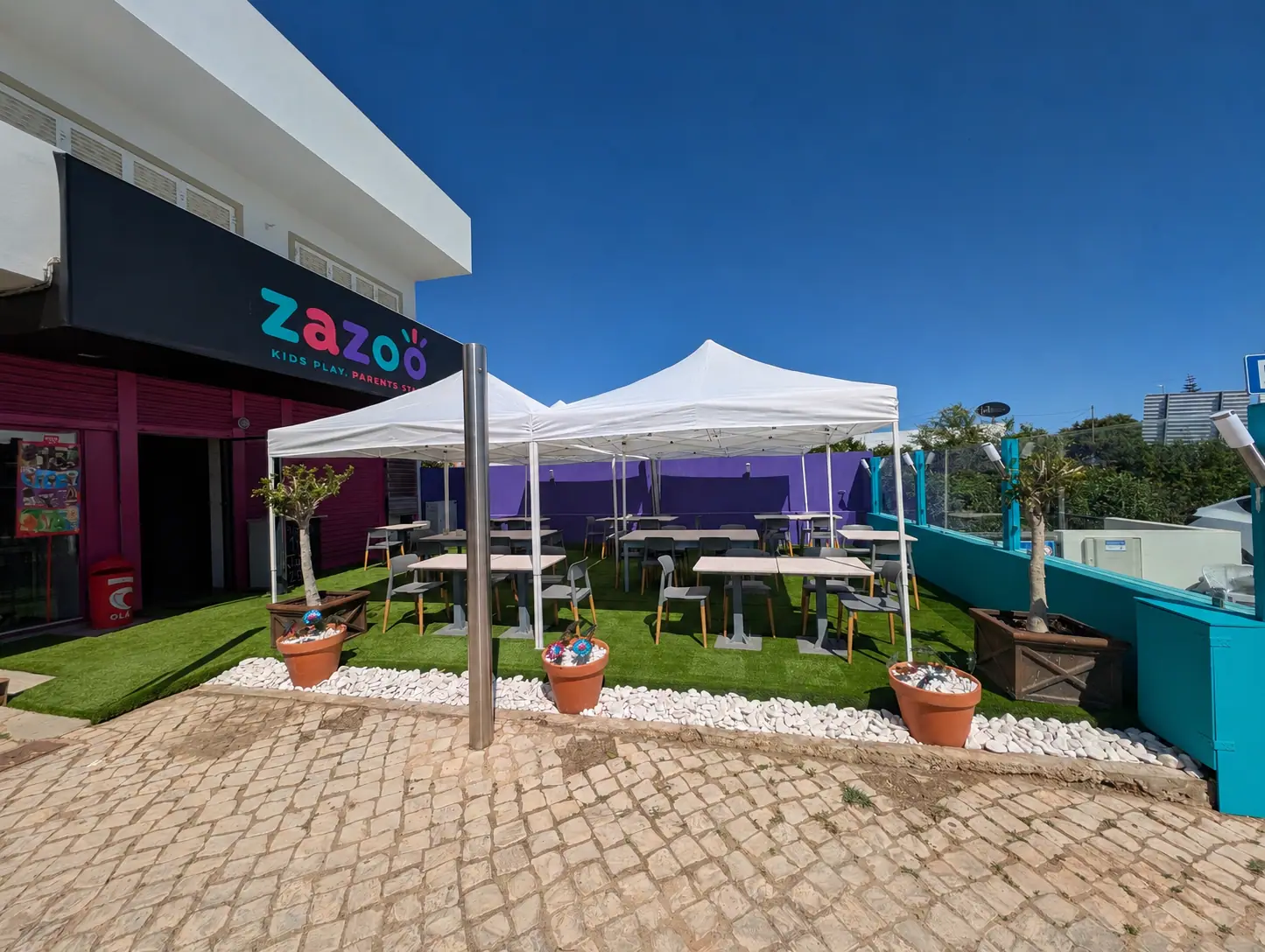 The exterior of Zazoo in Almancil: bright signage and a terrace of shaded tables