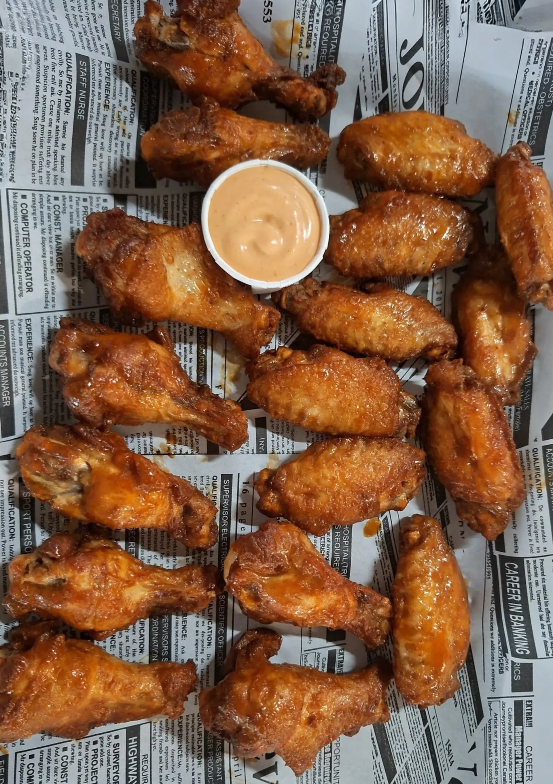 A newspaper-lined tray of crispy chicken wings with a creamy dipping sauce at Zazoo